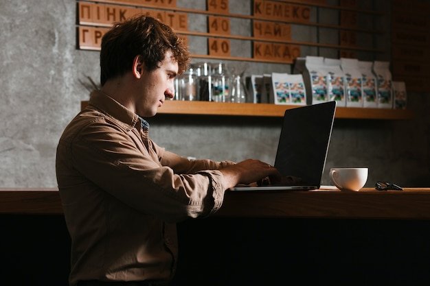 A person using CyberGhost VPN on a laptop while sitting in a coffee shop. The laptop screen shows the CyberGhost interface with a successful VPN connection indicated.