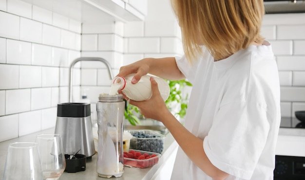 A medium shot of someone cleaning the Vitamix A3500 container in a kitchen sink. The container is filled with soapy water, and the person is using a long-handled brush to scrub the inside. The focus is on the brush and the container, with blurred background elements like the faucet and other kitchen utensils.