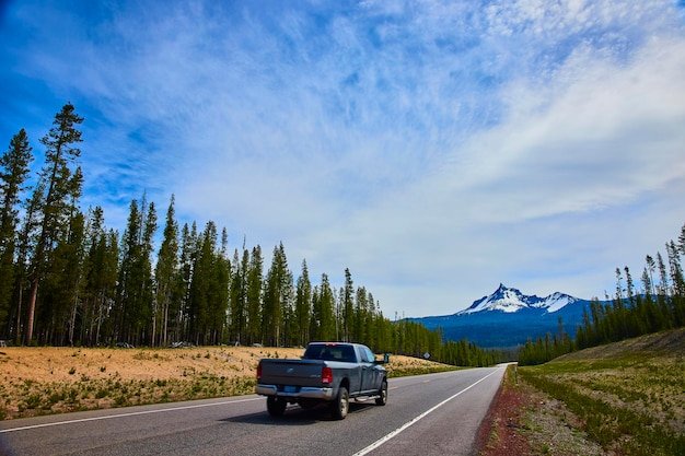 Ford F-150 Lightning 2025 towing a small travel trailer, driving on a highway with scenic mountain views in the background.